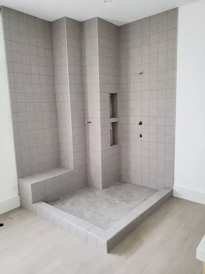 This walk-in shower remodel in Bullhead City includes a bench, recessed shelves, raised curb, and mosaic tile floor.