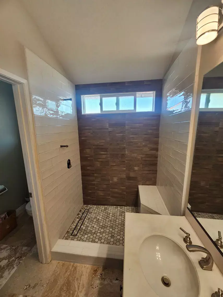 Fort Mohave bathroom remodel with walk-in shower, brown and white tiles, window, white sink, wall light, and vinyl plank flooring.