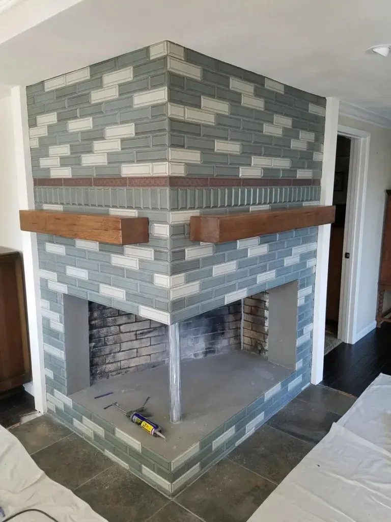 Double-sided corner brick fireplace with green and white tiles, wood mantels, and new vinyl flooring in Bullhead City remodel.