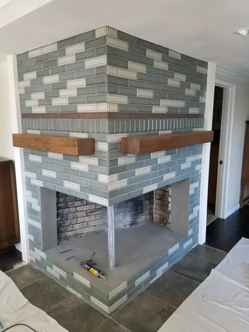 Double-sided corner brick fireplace with green and white tiles, wood mantels, and new vinyl flooring in Bullhead City remodel.
