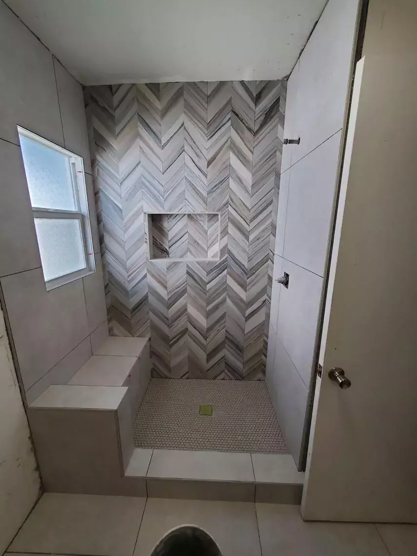 Modern shower with chevron accent wall, built-in bench, recessed shelf, window, and tile flooring in Bullhead City remodel.