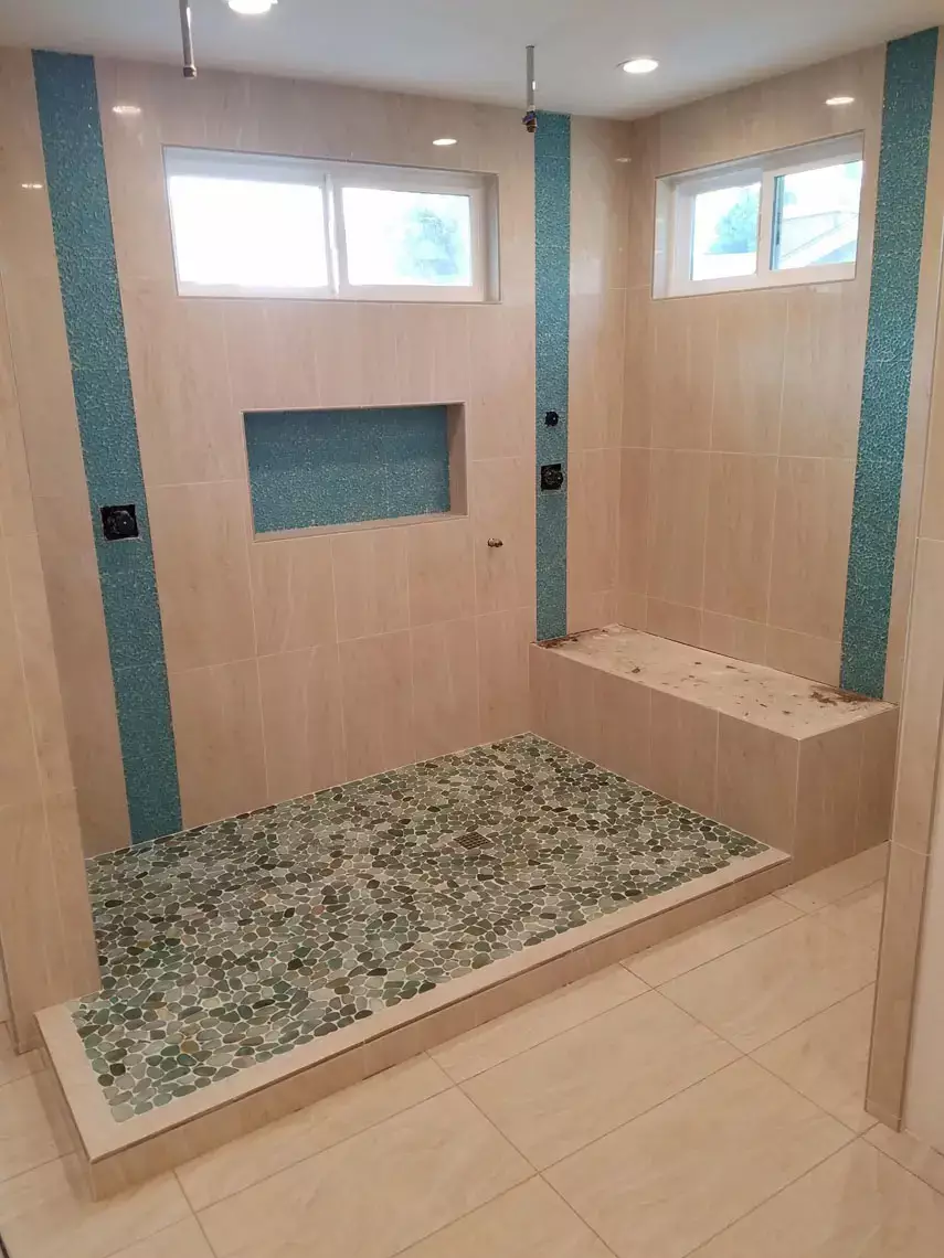Modern shower features beige tile walls, blue mosaic accents, built-in bench, shelf, and vinyl plank flooring in Bullhead City.