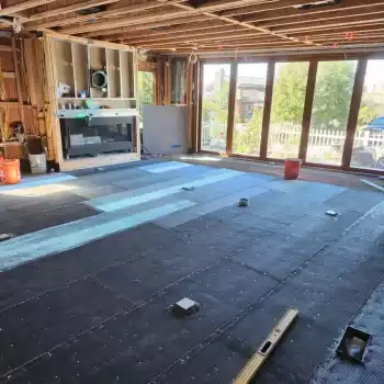 All Surfaces Flooring (13) Interior of a Bullhead City home under remodel with exposed beams, large windows, and flooring materials on the floor.