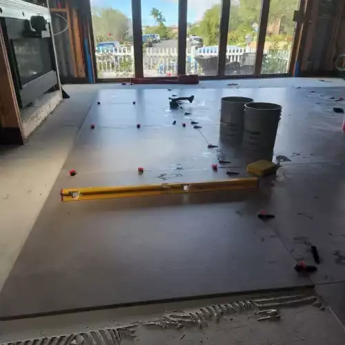 Large floor tiles are being installed for a kitchen remodel in Bullhead City, with tools and sliding doors to the outdoors.