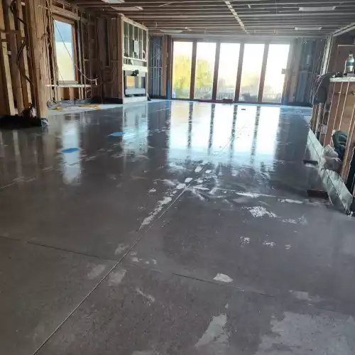 An unfinished room in Fort Mohave shows exposed framing, polished concrete, big windows, and visible flooring materials.