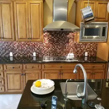 All Surfaces Flooring (2) Modern kitchen remodel in Fort Mohave with wood cabinets, black counters, mosaic tile backsplash, island sink, and sleek floors.