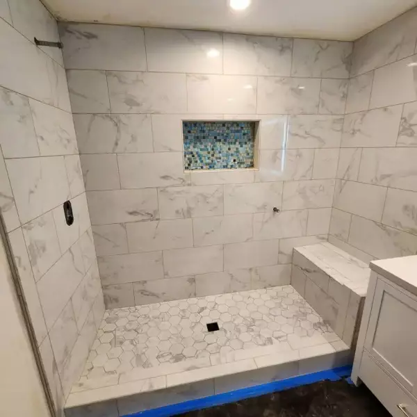 All Surfaces Flooring (9) Shower under construction in Bullhead City with white marble tiles, hex floor, bench, blue niche, and expert tile work.